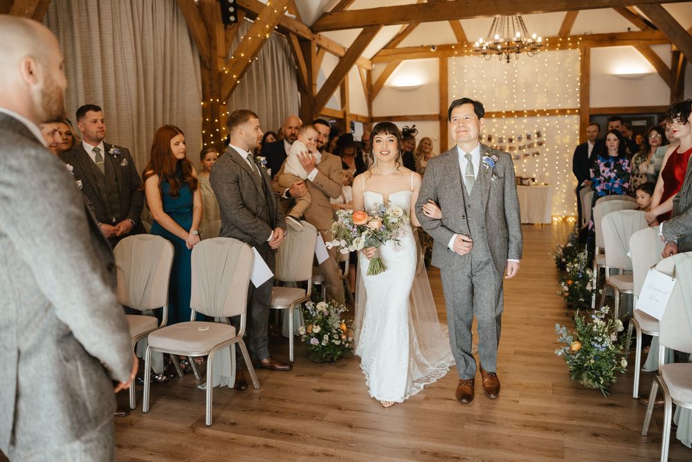 People dance and celebrate at a rustic barn wedding reception with exposed wooden beams and string lights.