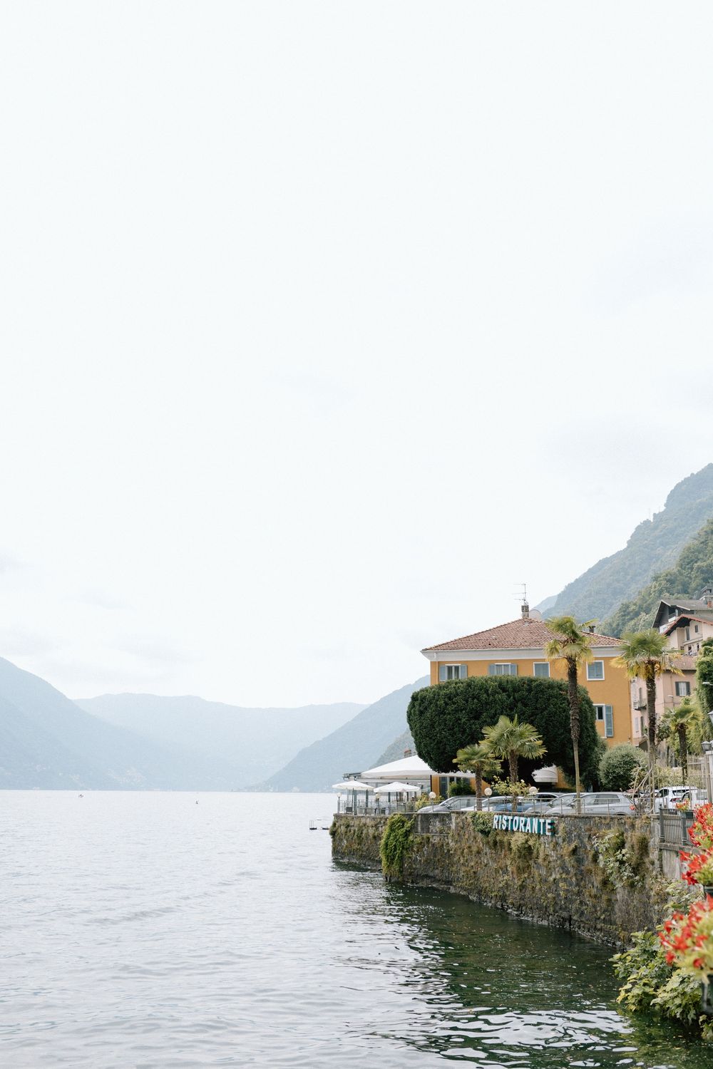 Scenic waterfront view of colorful buildings along Lake Como in Italy with misty mountains in the background.