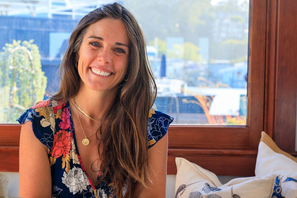 A person wearing a navy dress with floral details smiles while sitting near a window during daytime.