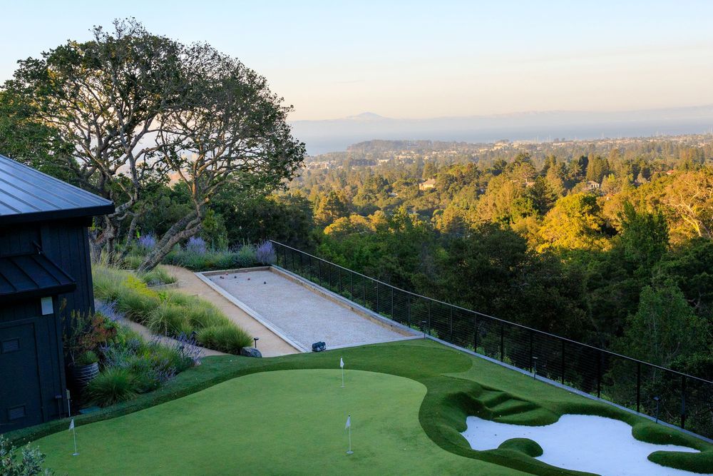 A private backyard bocce ball court and putting green overlooks a scenic valley at sunset from a hilltop vantage point.