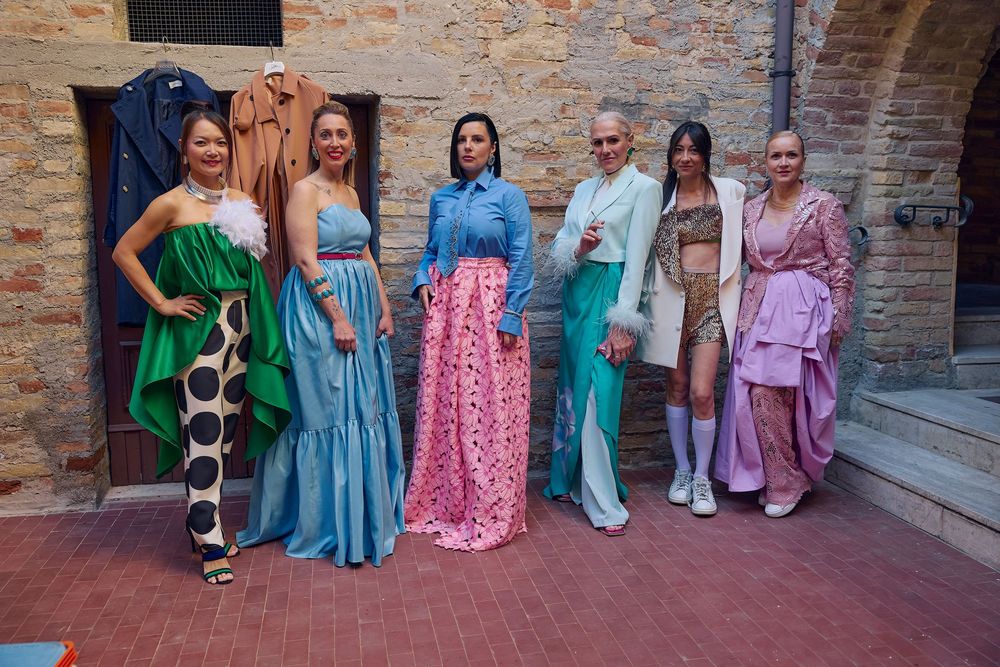 A group stands against a brick wall wearing colorful spring dresses in shades of green, blue, pink and pastel tones.