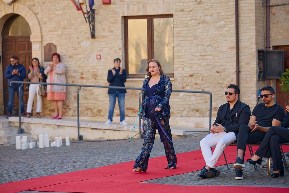 Tourists gather near a stone wall outside a historic building, with some people sitting on benches while others stand nearby.