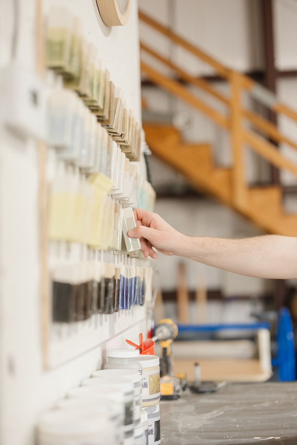 A hand reaches towards a row of glass vials in a laboratory setting with wooden stairs visible in the background.