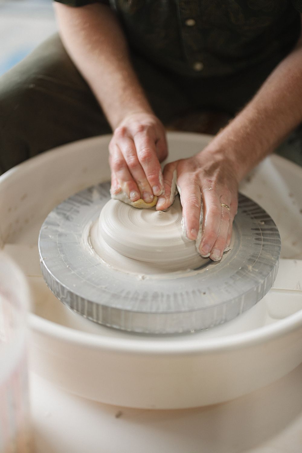 Hands shape clay on a pottery wheel while working on a rounded form with gentle pressure.