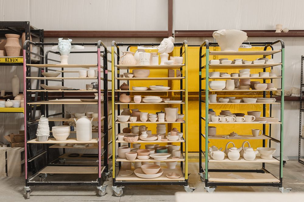 Organized storage shelves in a warehouse displaying white ceramic dishware and plates on multiple metal racks.