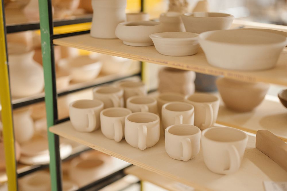 Rows of white ceramic cups and dishes displayed on shelves in a pottery workshop or retail store.
