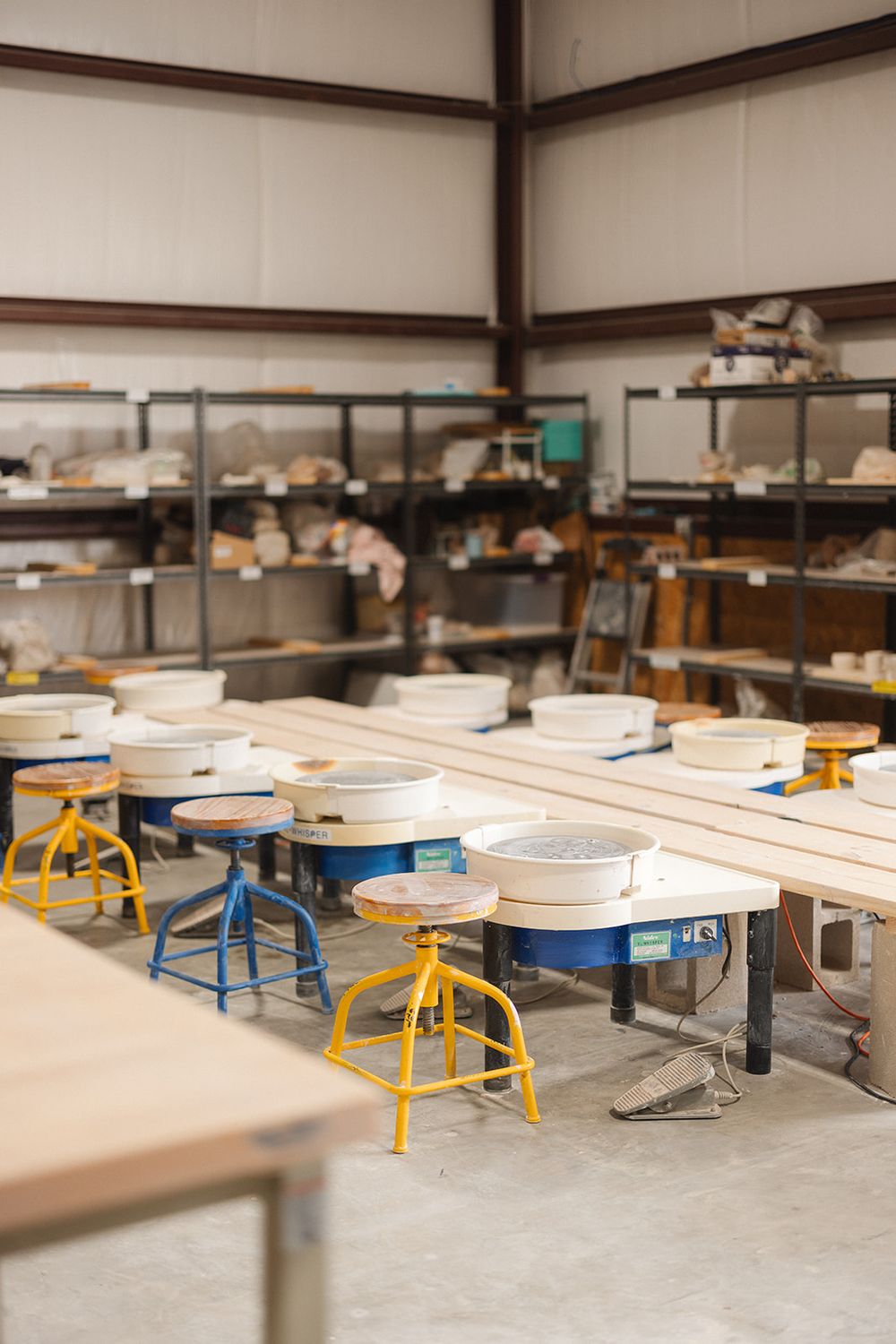 Industrial ceramics studio with rows of pottery wheels and yellow metal stools in a minimalist workshop space.