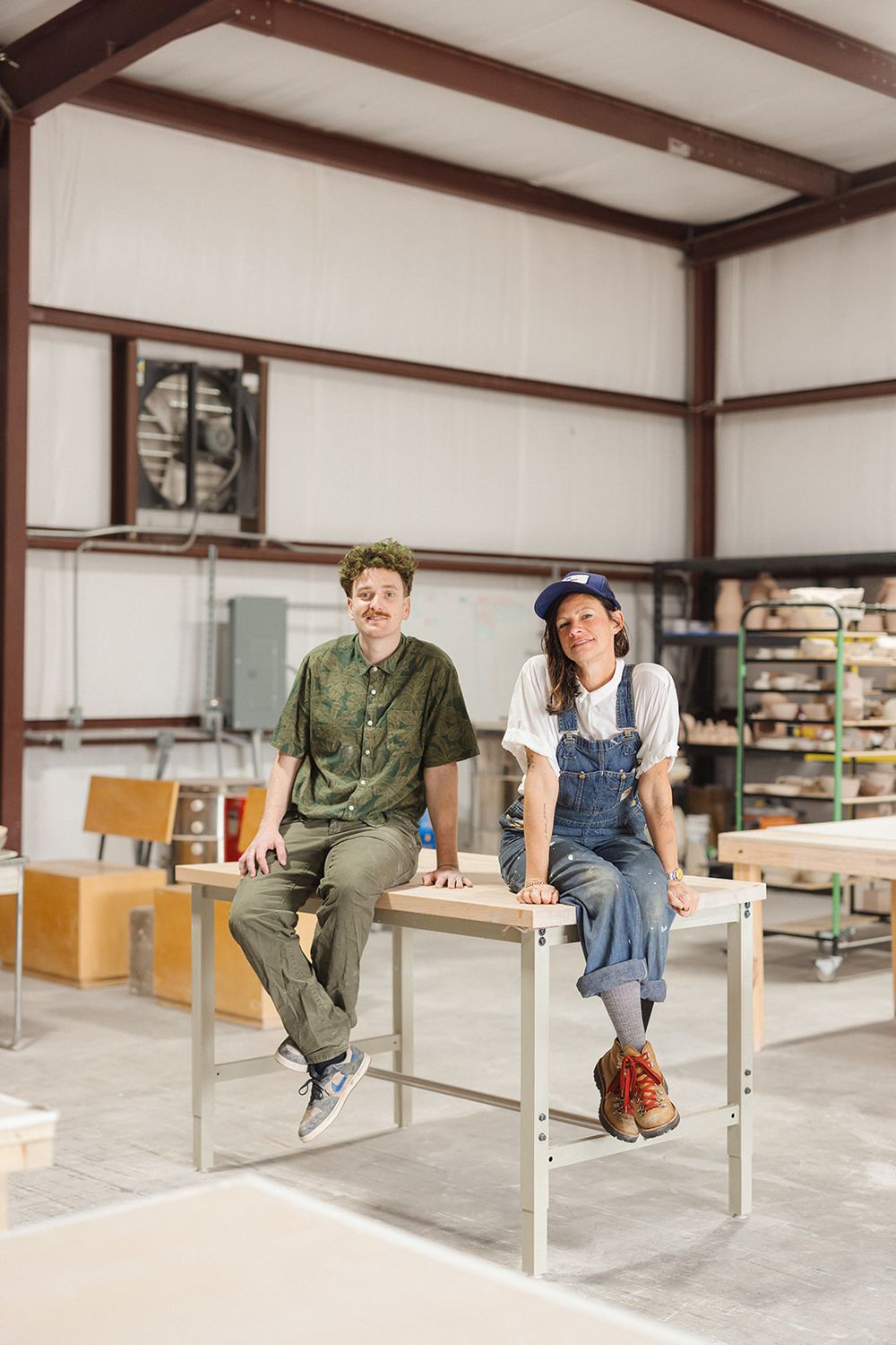 Three people sit casually on modern white chairs in an industrial studio space with exposed beams overhead.