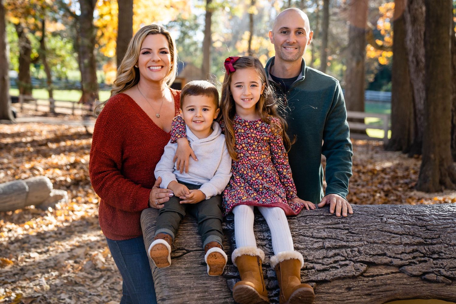 A happy family poses outdoors among autumn trees during a casual photo session in a park.