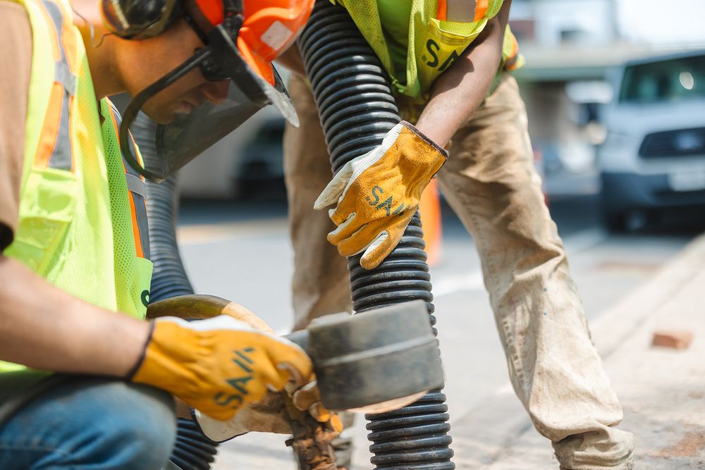 Construction worker in safety vest uses heavy-duty power tool to drill into concrete ground during maintenance work.