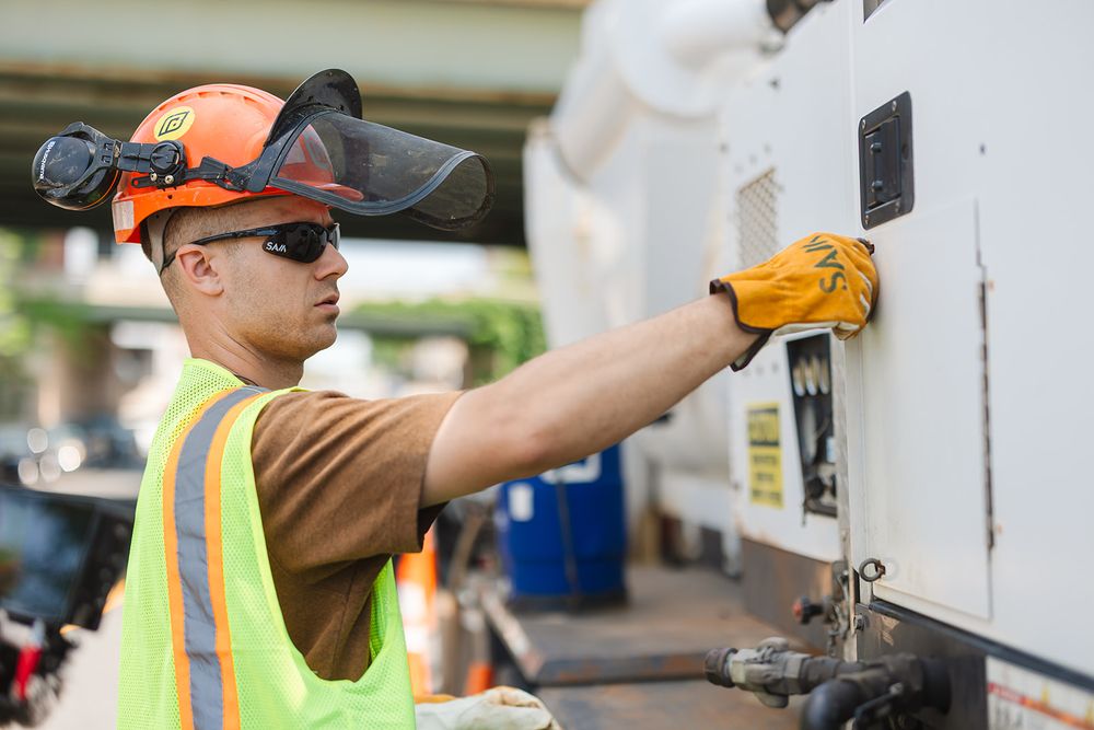 Worker in safety gear and hard hat operating equipment on construction site.