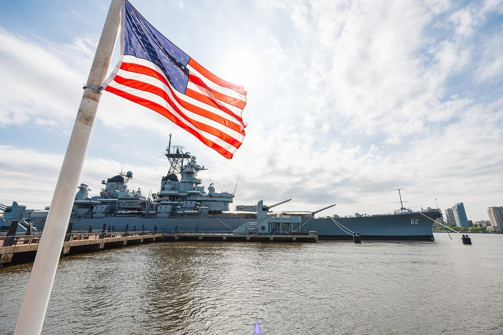 American flag waves in front of the USS New Jersey battleship museum docked at the Camden waterfront on Delaware River.