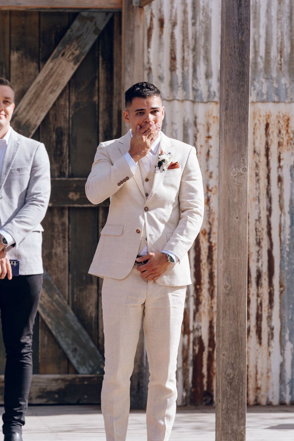 Groom in cream suit shows emotional reaction during wedding ceremony.