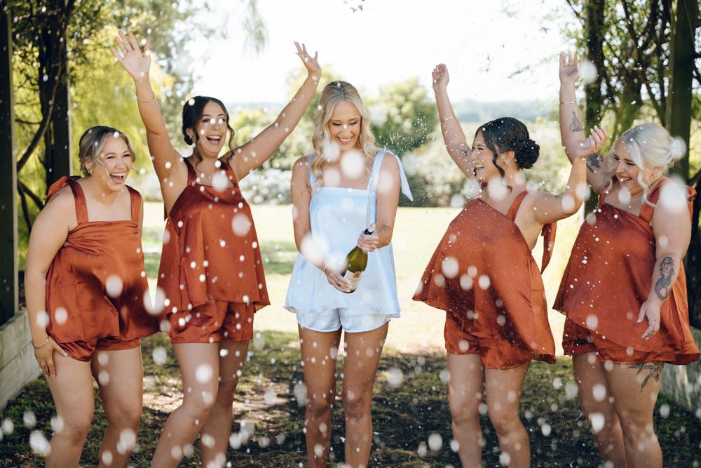 Celebration with bridesmaids in rust-colored dresses throwing confetti in outdoor setting.