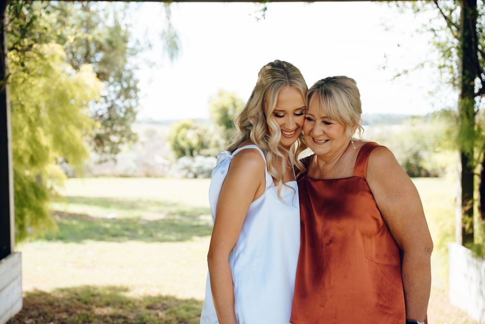 Wedding photography captures candid moment between women in white and rust-colored dresses outdoors.