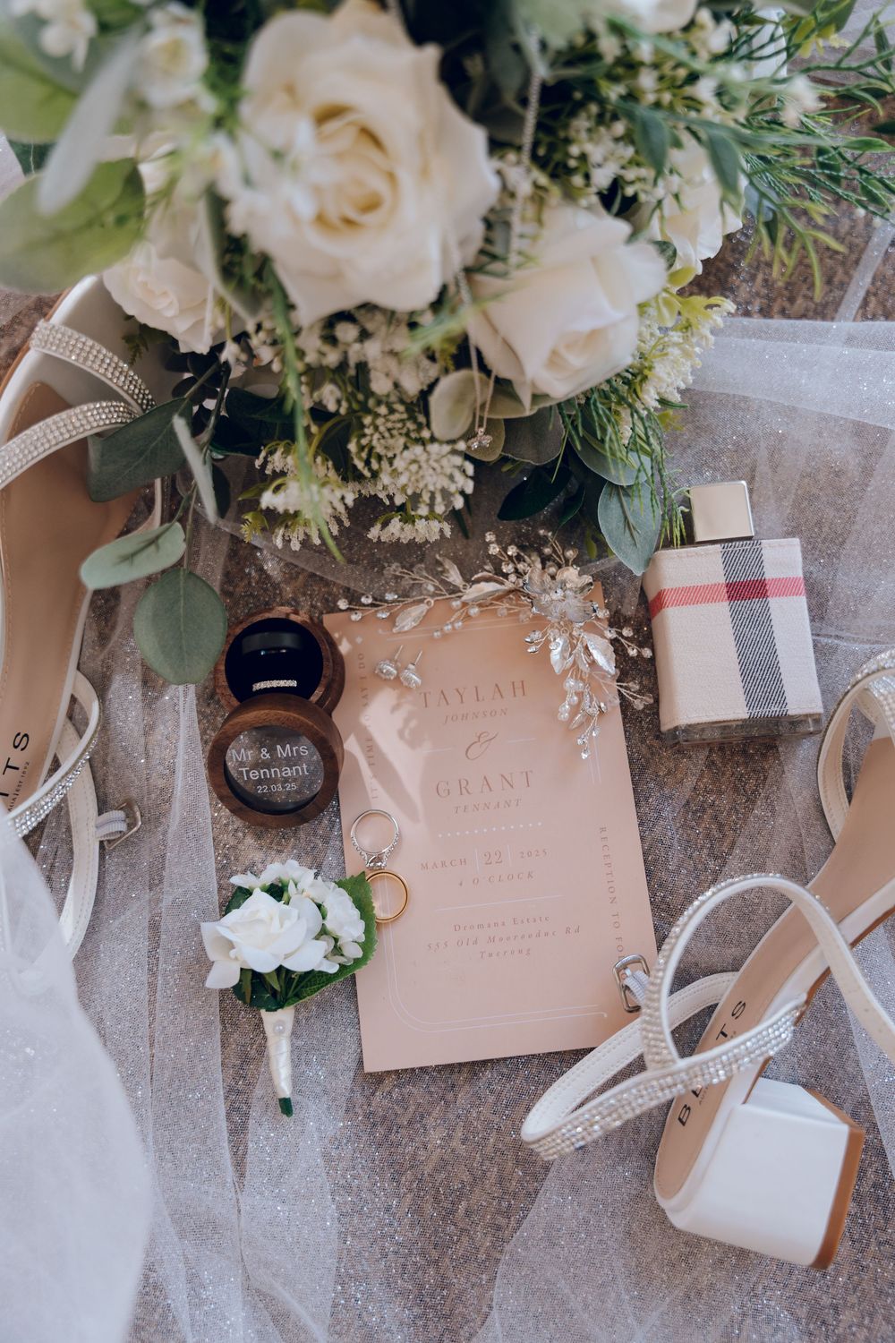 Wedding details flatlay with roses, invitation, rings and accessories on tulle fabric.