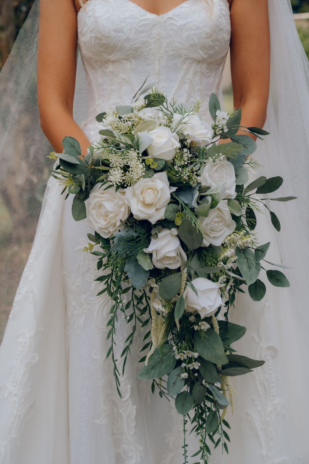 Cascading white rose and eucalyptus bridal bouquet held against lace wedding dress.