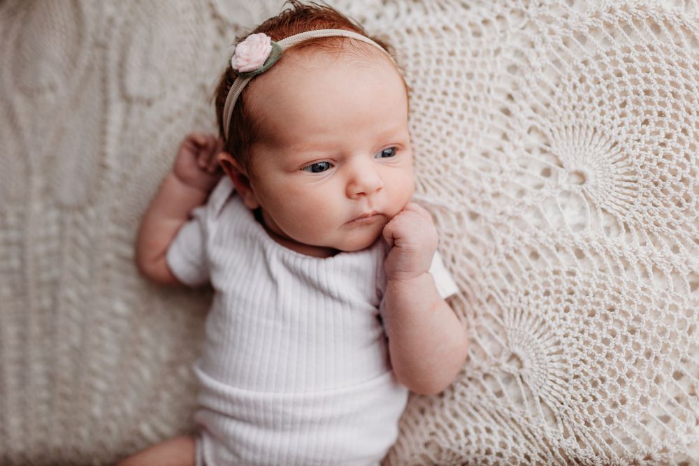 Baby in white clothing resting peacefully on delicate lace pattern blanket.