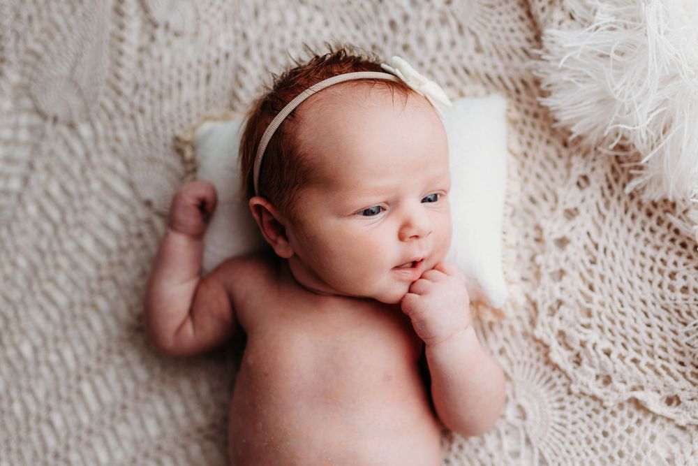 Infant wearing white outfit rests on textured cream-colored surface during a photo session.