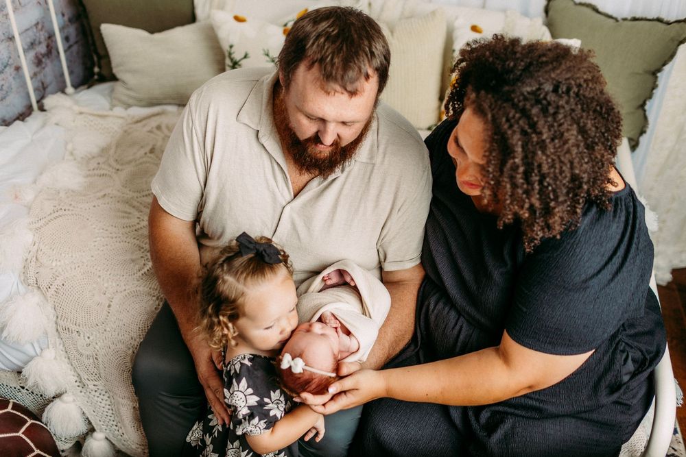 Intimate candid family moment of parents cuddling with their newborn on a cozy sofa.