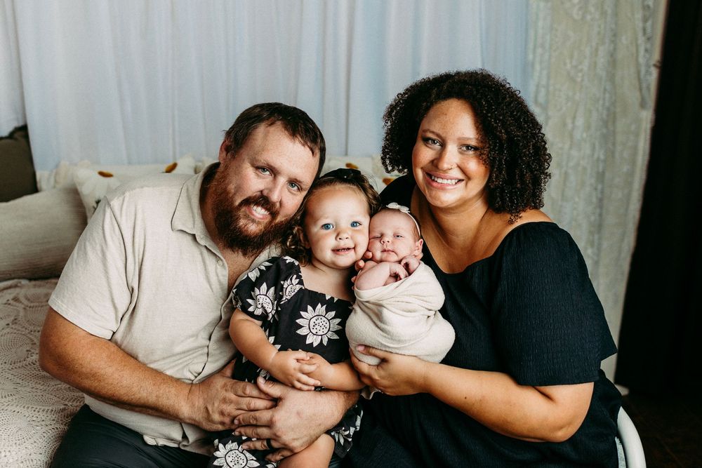 A family of four poses together on a couch for an intimate portrait session against a white backdrop.
