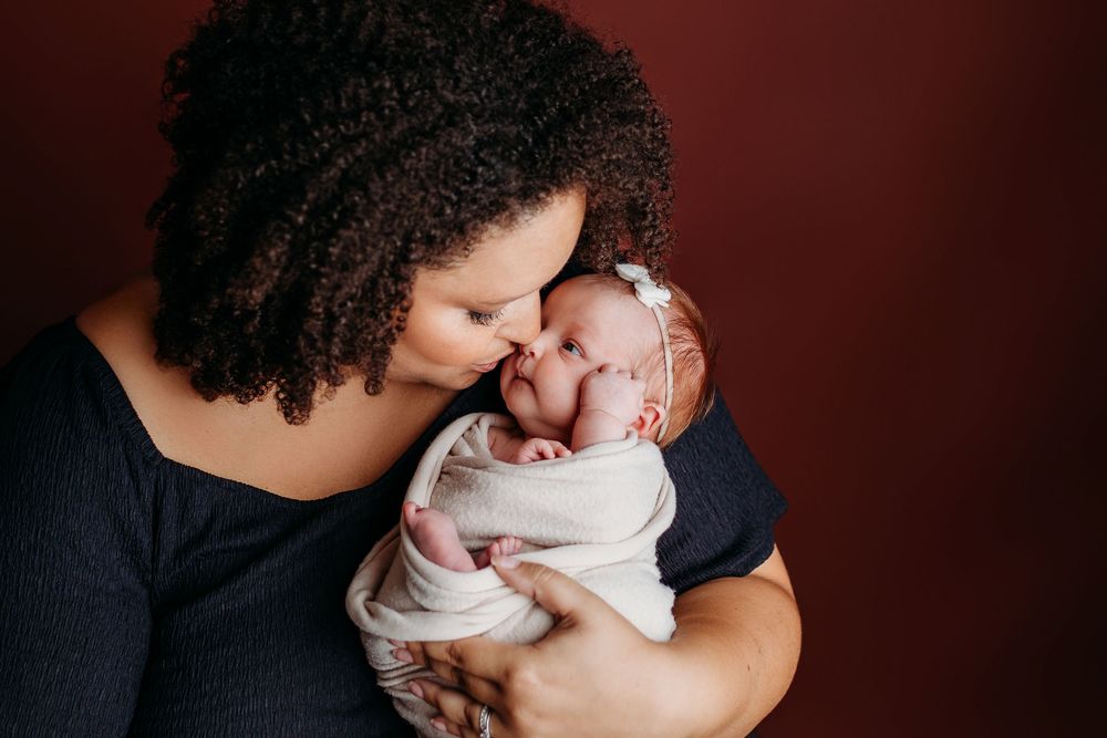 Family lifestyle photos against burgundy backdrop showing tender moments with newborn.