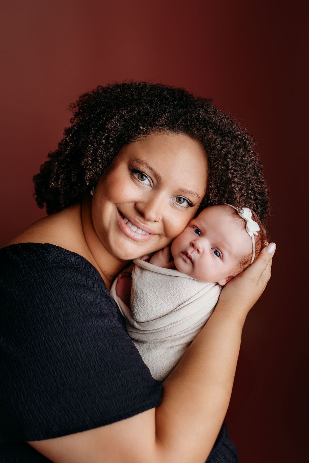 Heartwarming studio portrait series with dark burgundy background showing tender embraces.