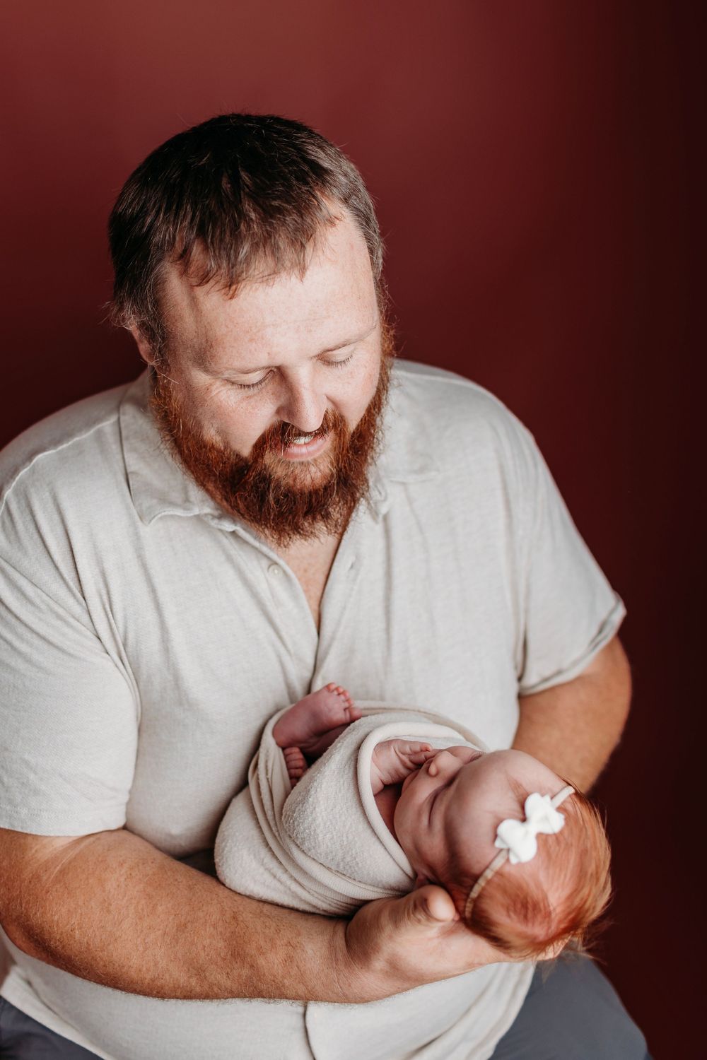 Studio portraits against burgundy backdrop show tender moments and gentle interactions with infant.