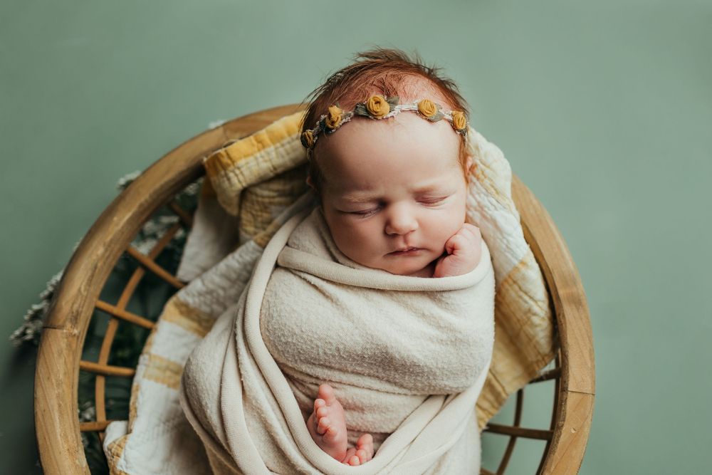 Professional newborn photography session with baby wrapped in white on mint green background.