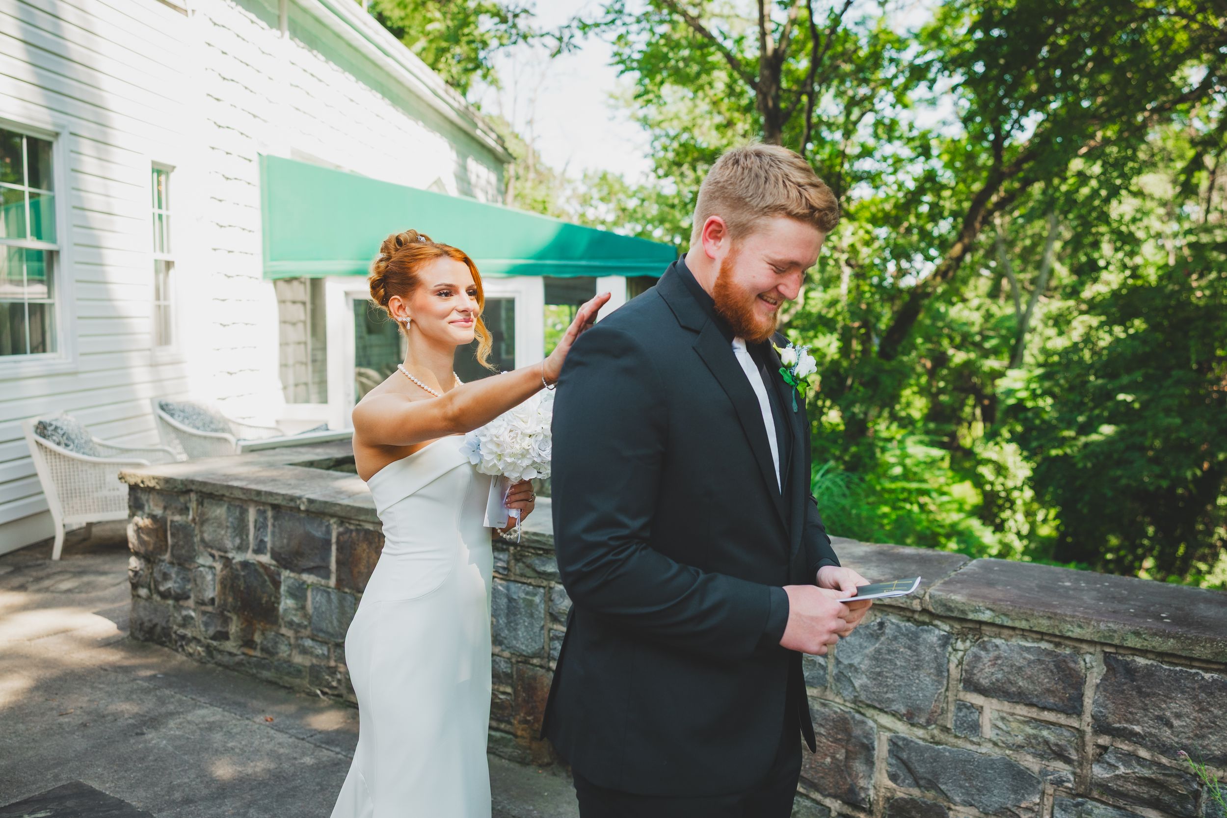 A bride playfully points at the groom's back while standing on a stone patio during their wedding day for their first look photo session