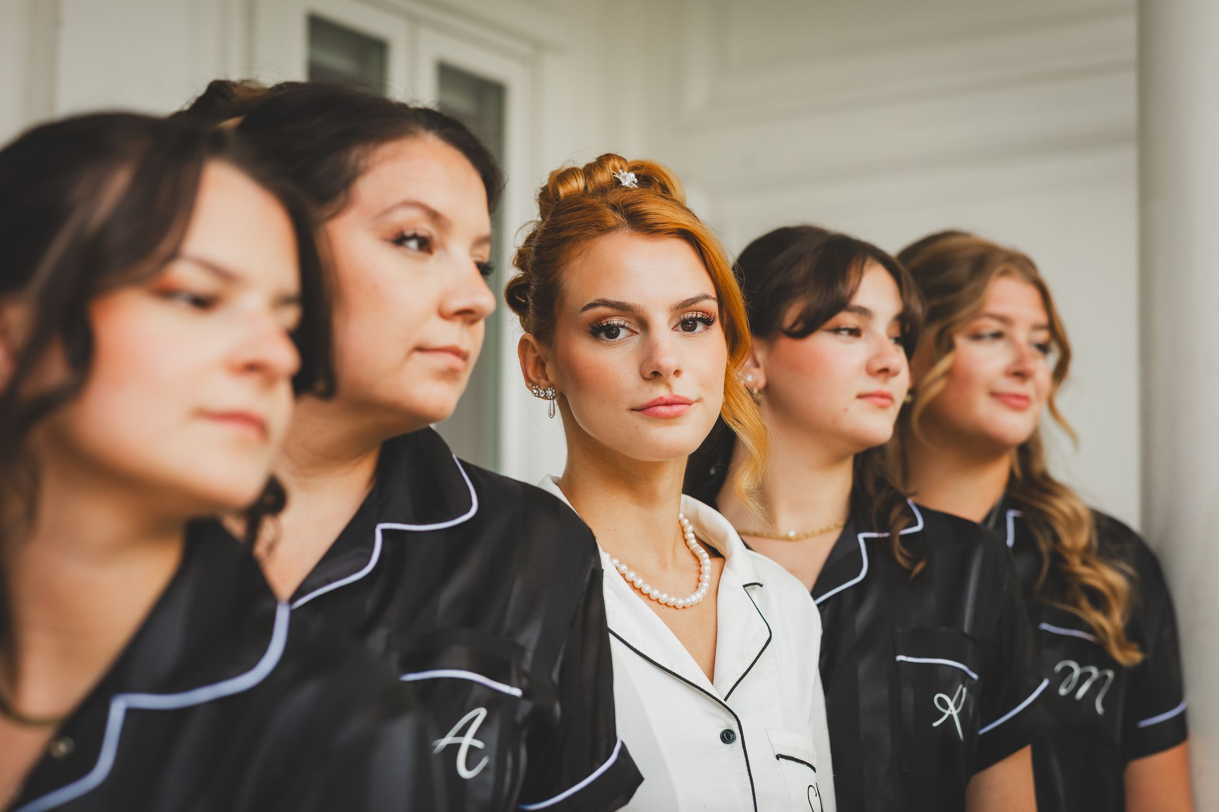 Bride and Bridesmaid wearing matching black and white piped pajamas stand together in a line looking to the side.