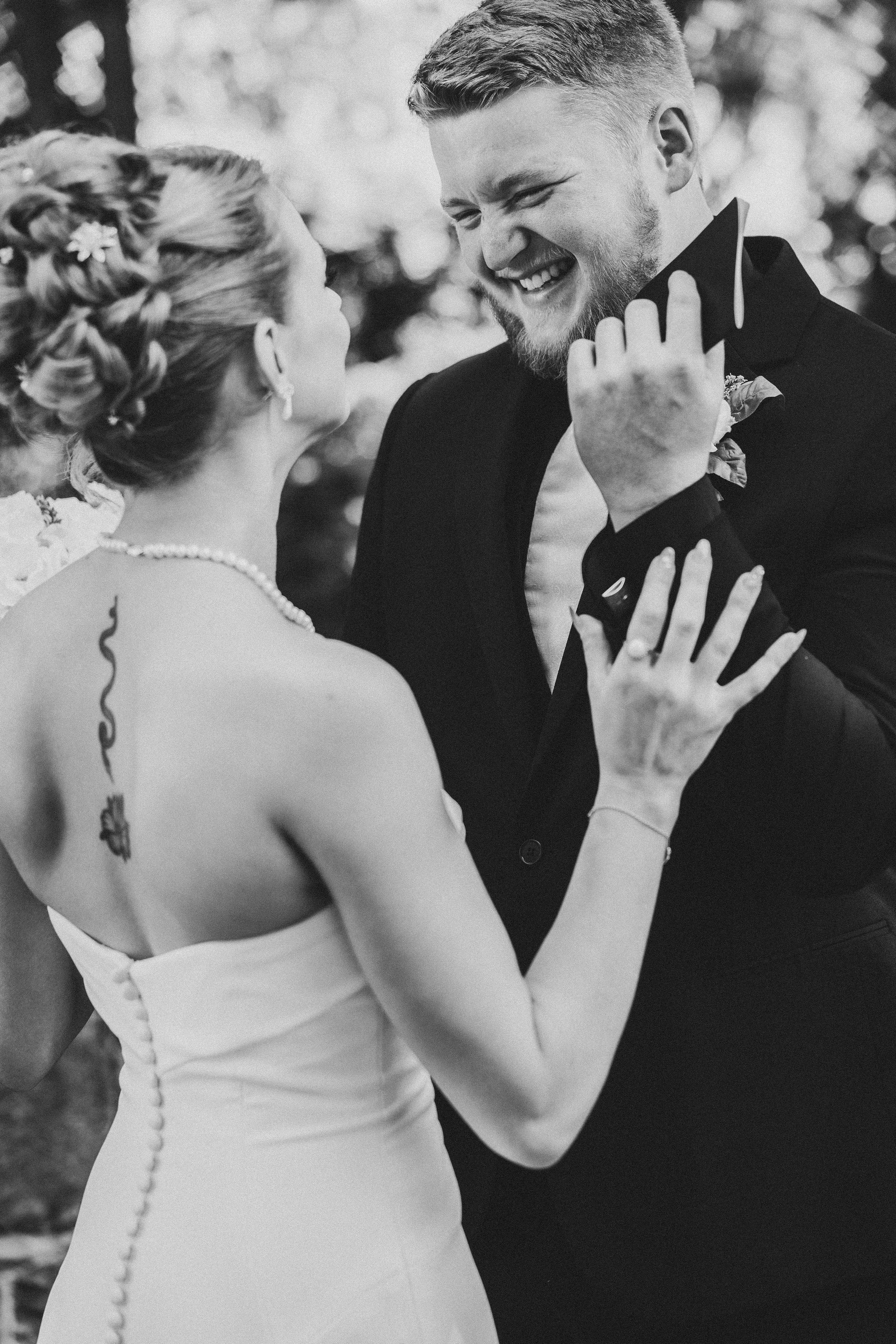 A candid black and white wedding moment captured as bride and groom share a laugh during their first look photo session