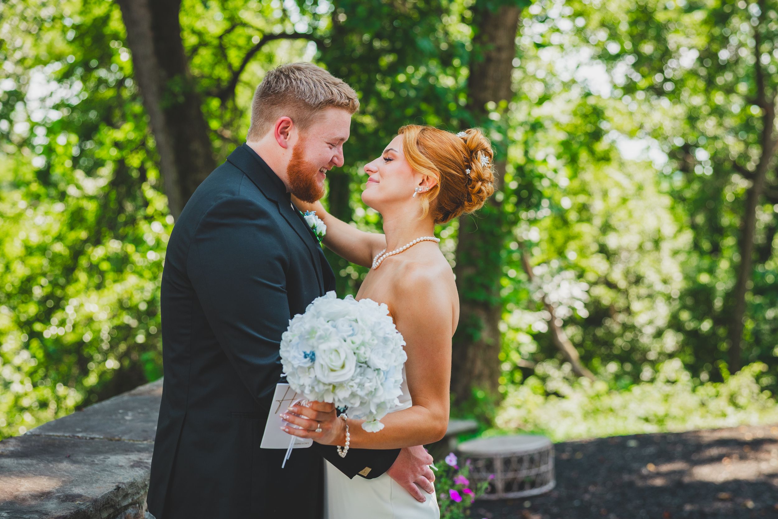 Bride and groom outdoors on their wedding day surrounded by lush green trees.