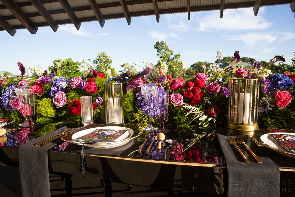 Elegant wedding table setting with vibrant pink and red floral arrangements and gold candle holders.
