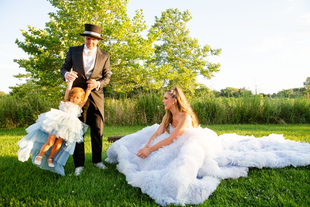 A couple celebrates outdoors on lush grass with a saxophone player performing in formal attire at a sunny outdoor event.