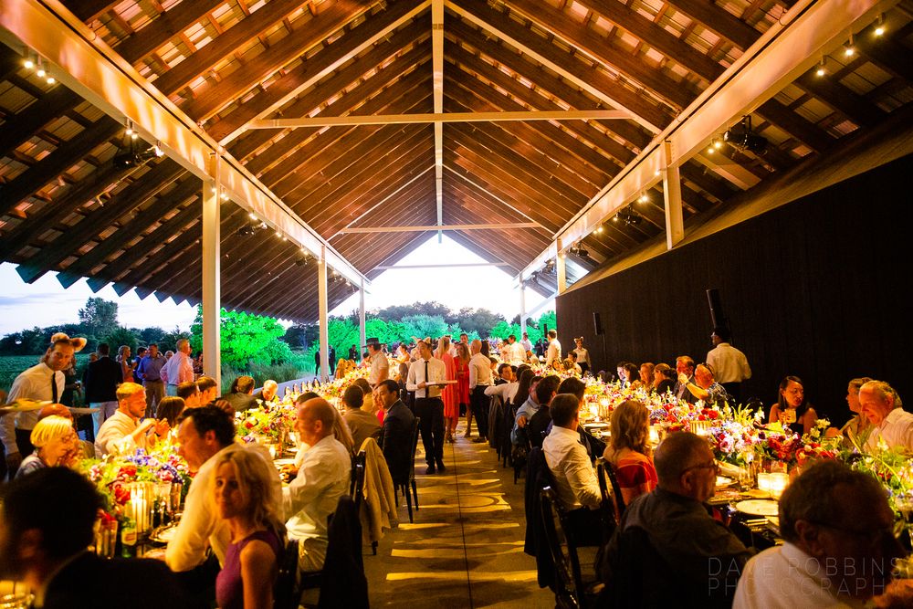 Evening dinner event under a rustic wooden pavilion with long tables filled with guests enjoying a communal meal.