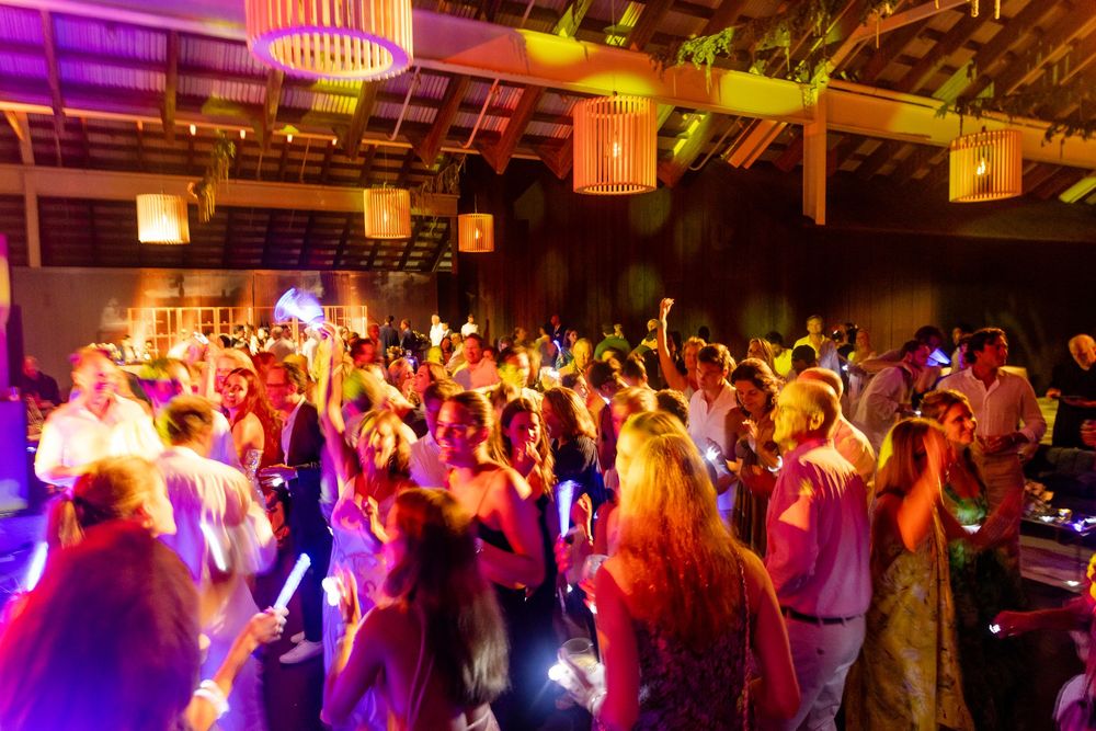 Crowded dance floor with colorful purple and yellow lighting at a nighttime celebration.