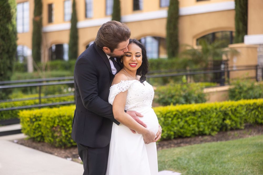 A romantic couple embraces and dances together on the grounds of an elegant brick building surrounded by manicured gardens.