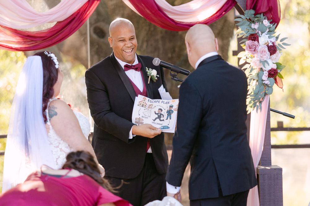 An outdoor wedding ceremony under pink and white fabric draping with an officiant and couple at the altar.