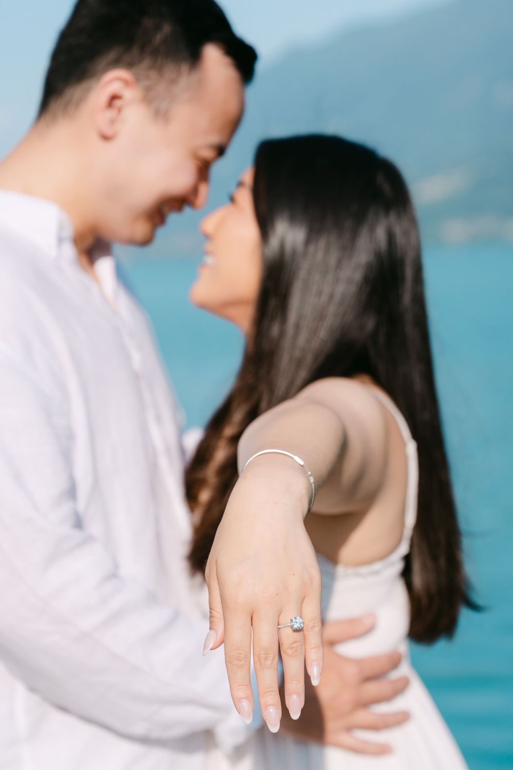 A romantic couple sharing an intimate moment by turquoise waters, with the bride showing off her engagement ring.