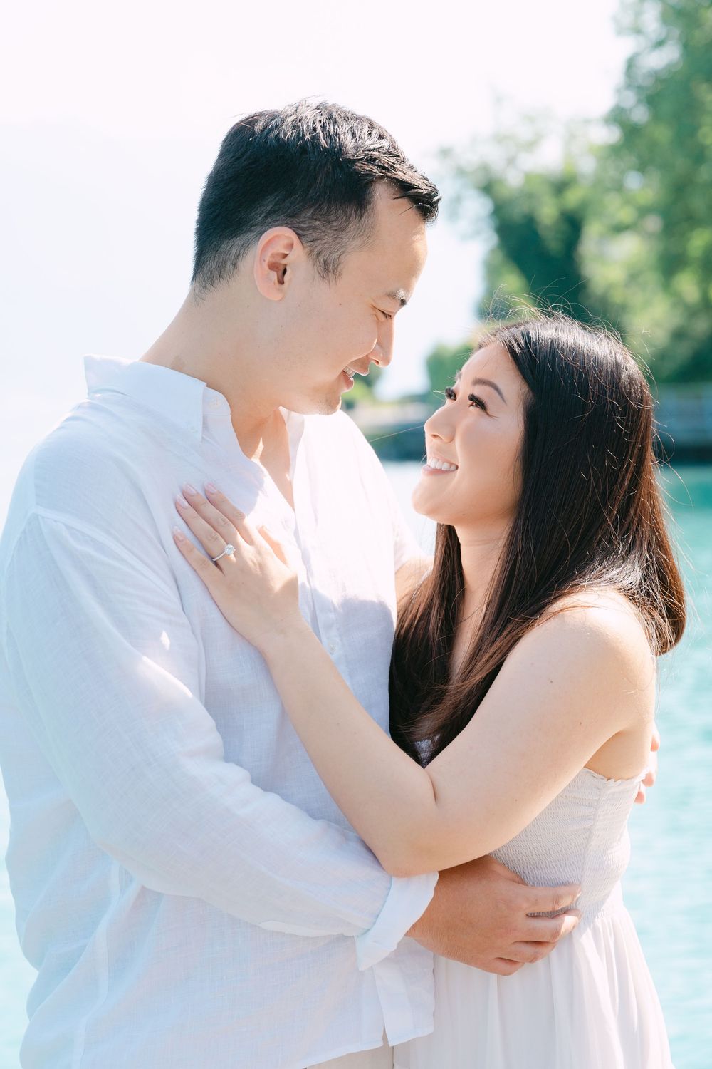 A romantic couple in white embracing outdoors during a bright sunny day.
