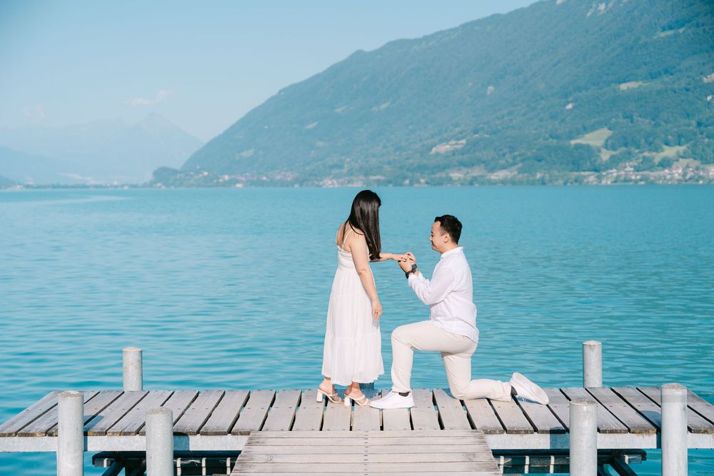 A romantic proposal scene on a wooden dock overlooking a scenic mountain lake with turquoise waters.