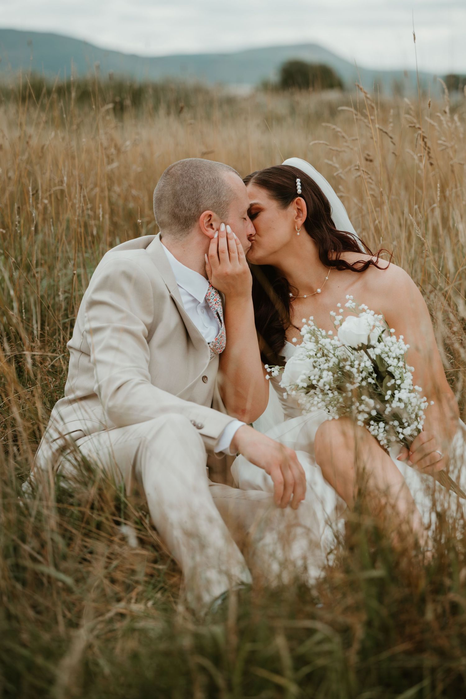 A newlywed couple shares intimate moments in a golden field of tall grass during their rustic outdoor wedding.