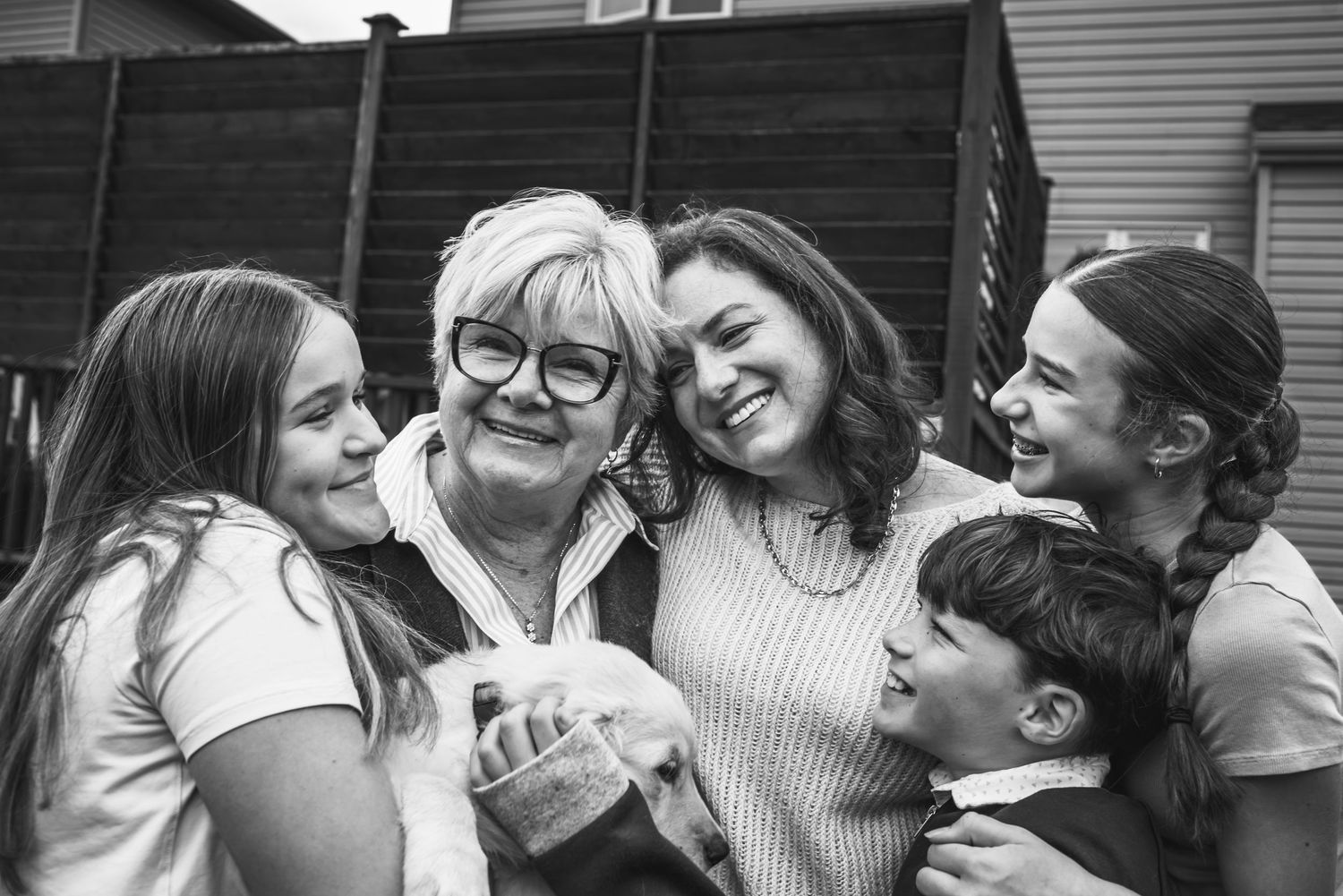 Group of family share smiles and laughter in a black and white candid photo outside a building.