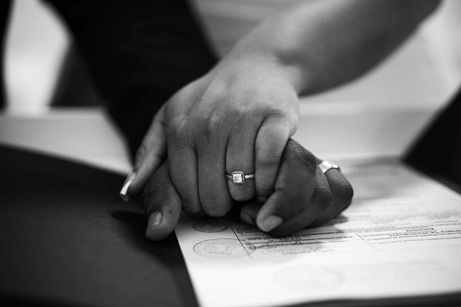 A close-up black and white photo of hands wearing a wedding ring resting on document papers.