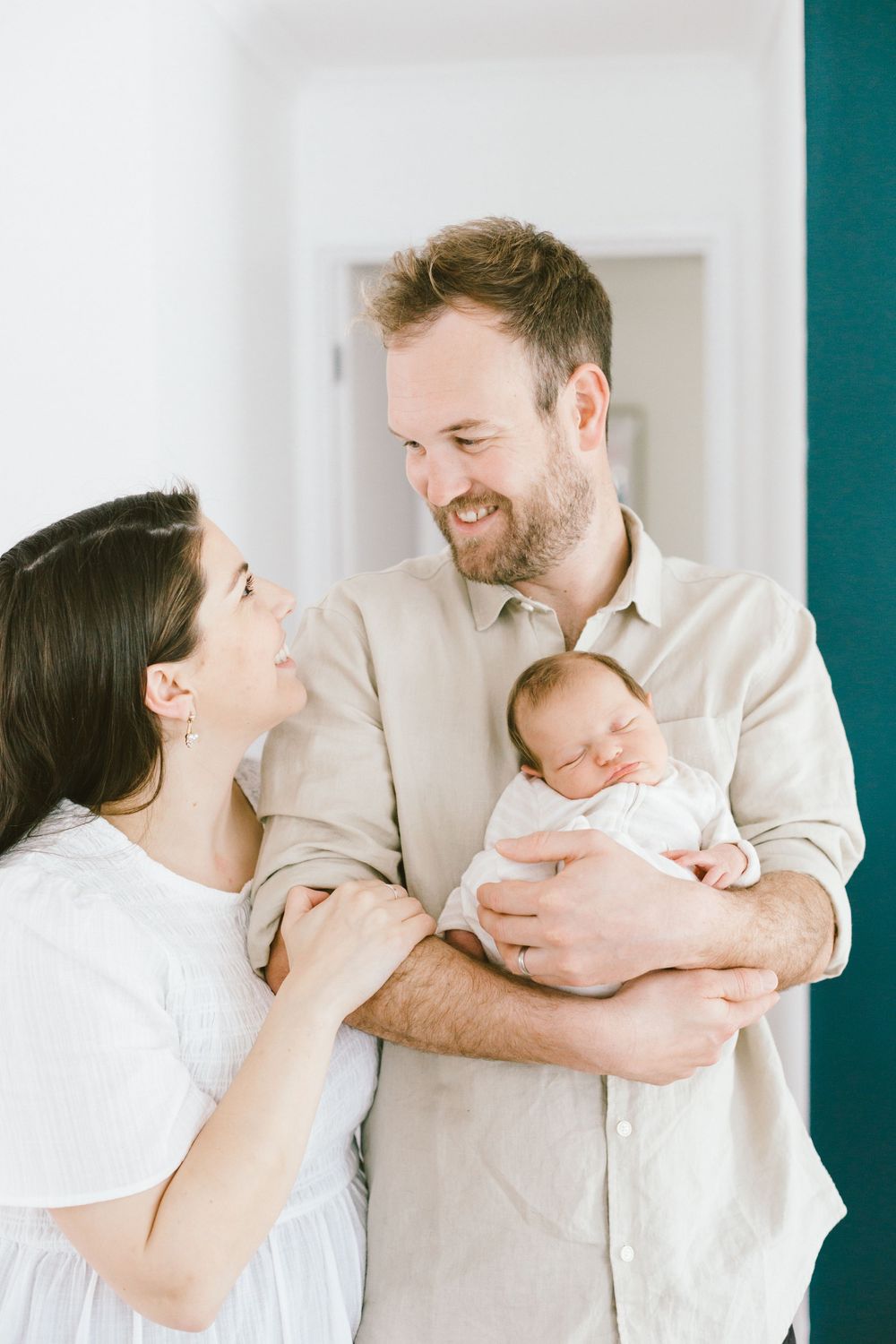 Parents share tender moment with newborn baby against teal and white interior wall.