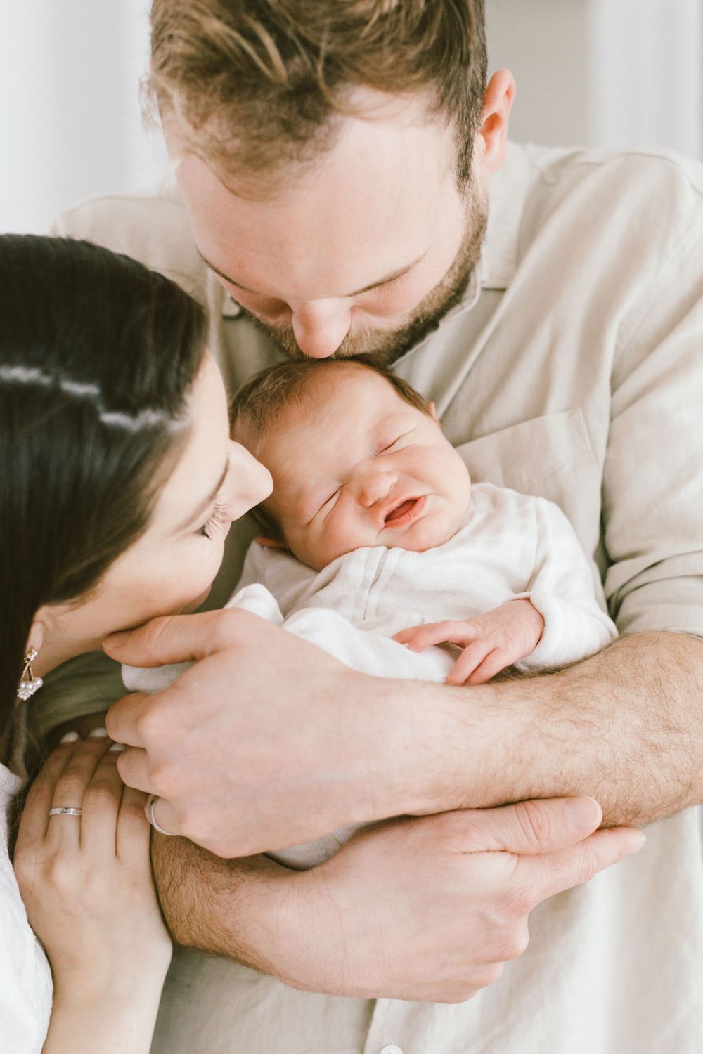 Parents sharing gentle kisses with their sleeping newborn baby.