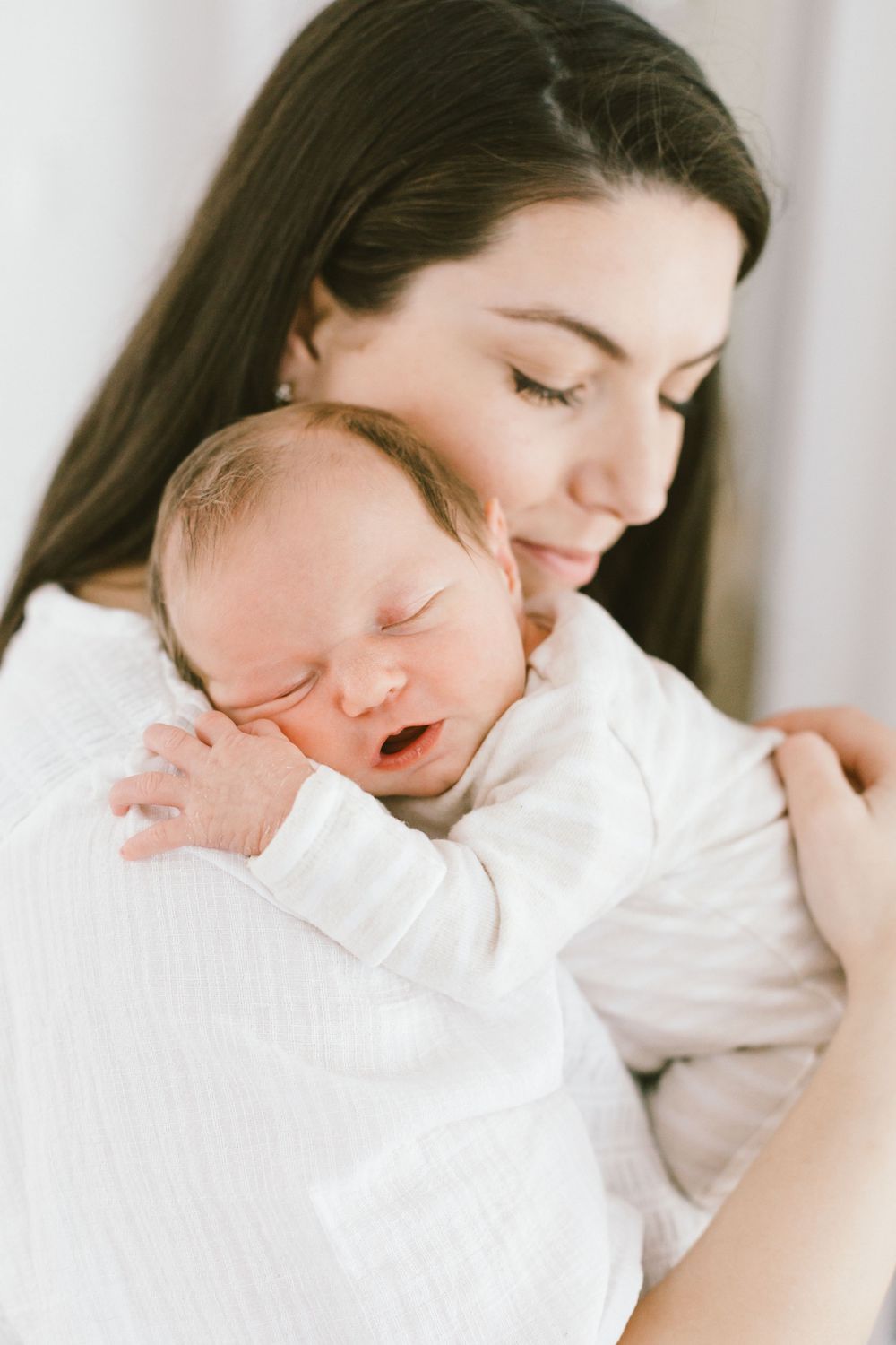 Peaceful moment between parent and sleeping newborn baby dressed in white.