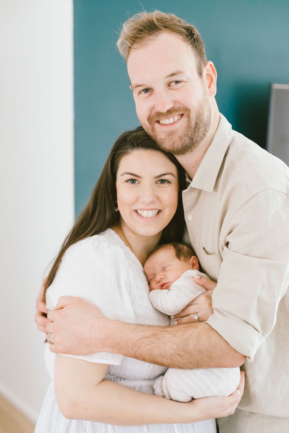 Family portrait with sleeping newborn against teal wall interior.