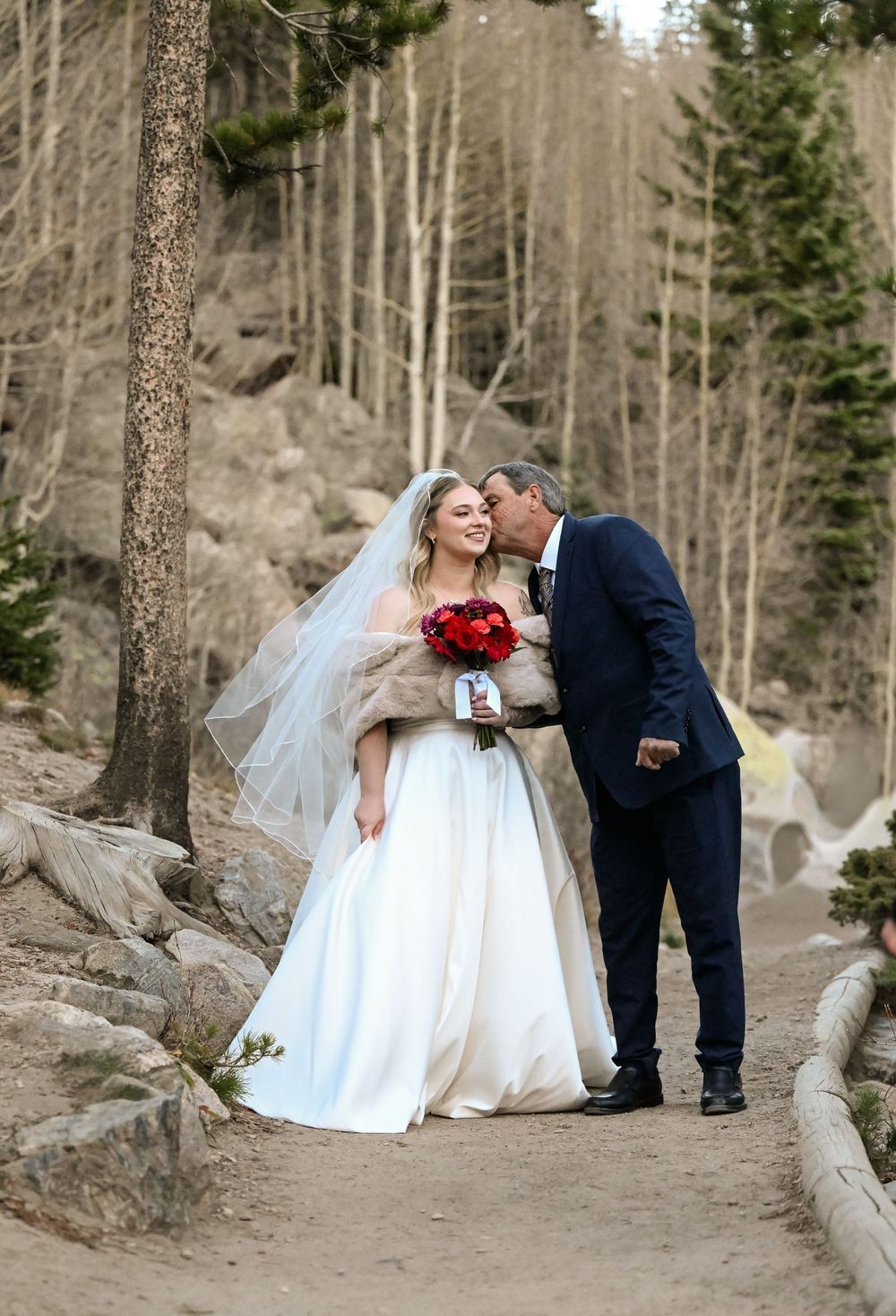 A romantic winter wedding couple sharing an intimate moment on a forest path surrounded by aspen trees and snow.
